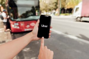 A person using a smartphone to open the Uber app while standing near a city street, illustrating the convenience of ride-hailing services often linked to credit cards with benefits like cashback, discounts, or travel rewards.