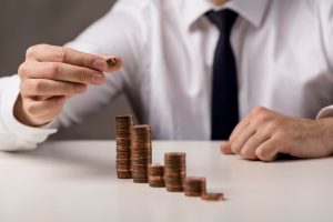 A man in business attire stacking small piles of coins in ascending order, symbolizing gradual financial growth and the accessibility of wealth-building through fractional investments.