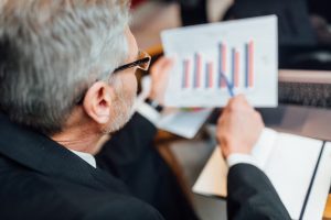 A mature businessman analyzing a printed bar chart with a pen in hand, illustrating strategic financial planning and performance tracking related to medium-term investments.